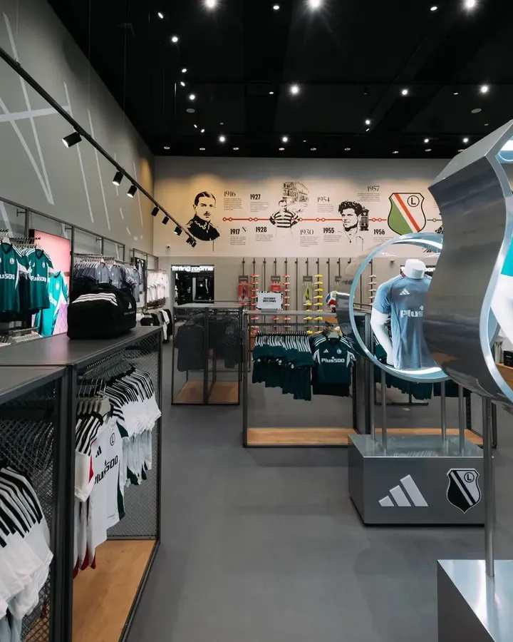 Wnętrze fanstore Legii z koszulkami, gadżetami i historią klubu na ścianie